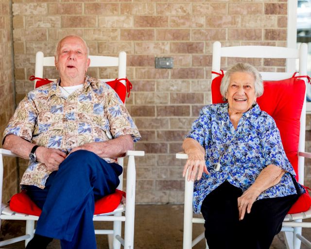 Gardens at Columbine residents laughing in white rocking chairs on the brick porch