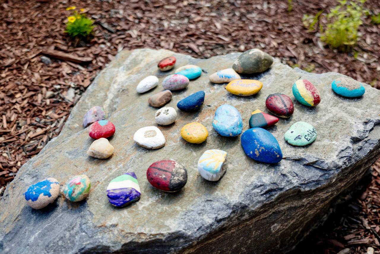 Painted memorial rocks arranged on a boulder in the Gardens on Quail garden