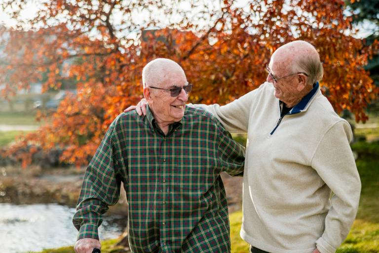 Two Golden Pond residents laughing together beneath an autumn red tree