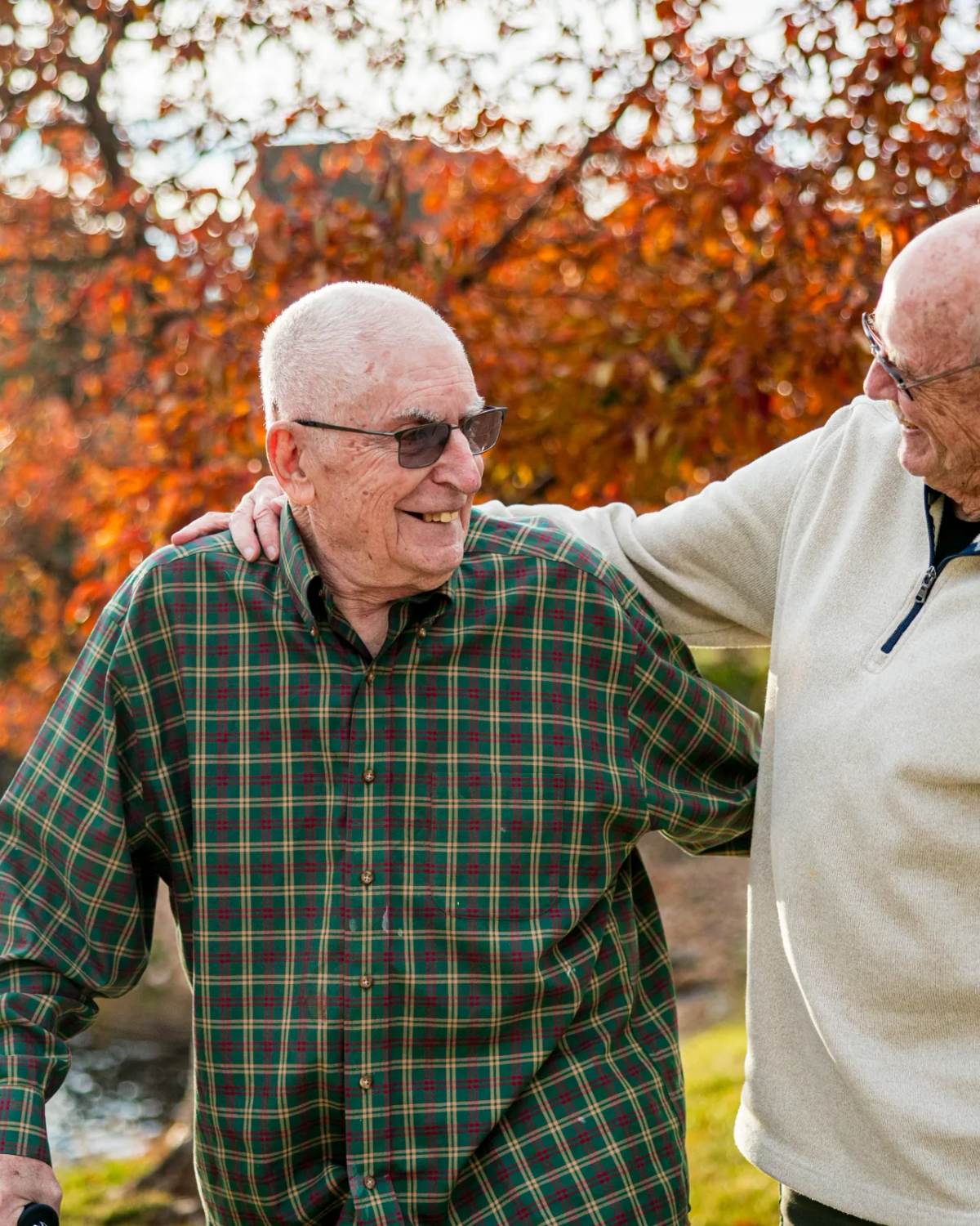 Two Golden Pond residents laughing together beneath an autumn red tree