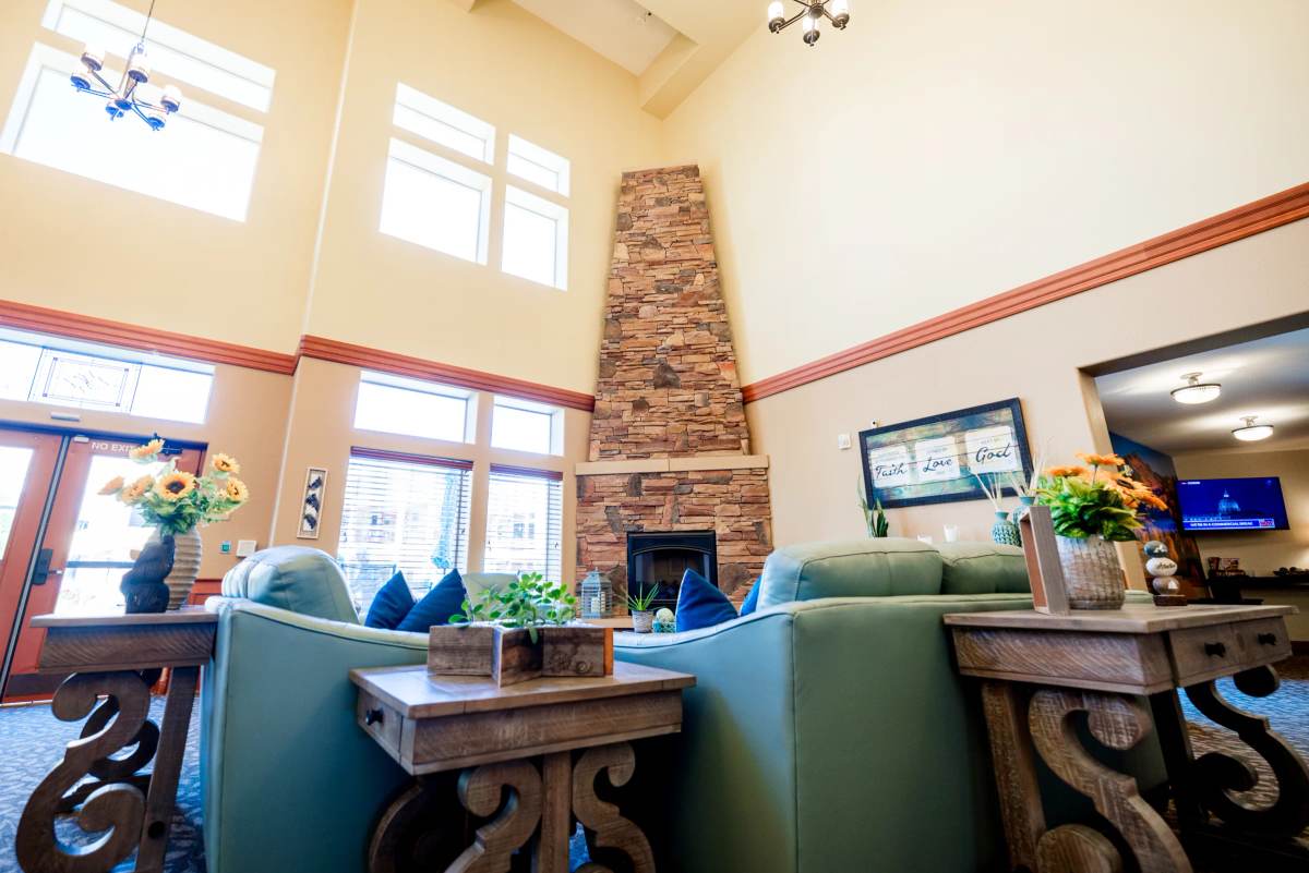 Gardens on Quail great room with tall stone fireplace, green sofas, and sunflowers