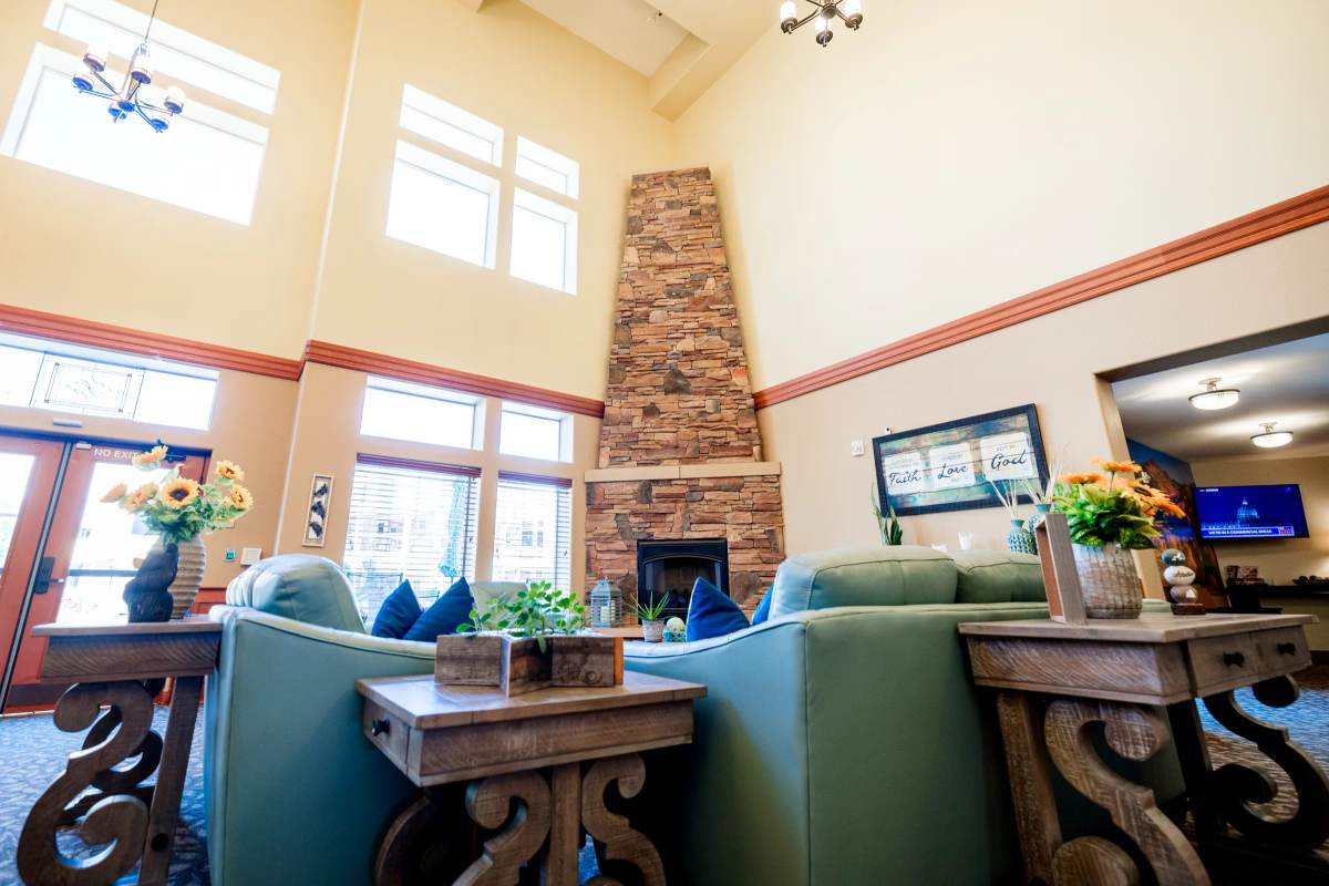 Gardens on Quail great room with tall stone fireplace, green sofas, and sunflowers