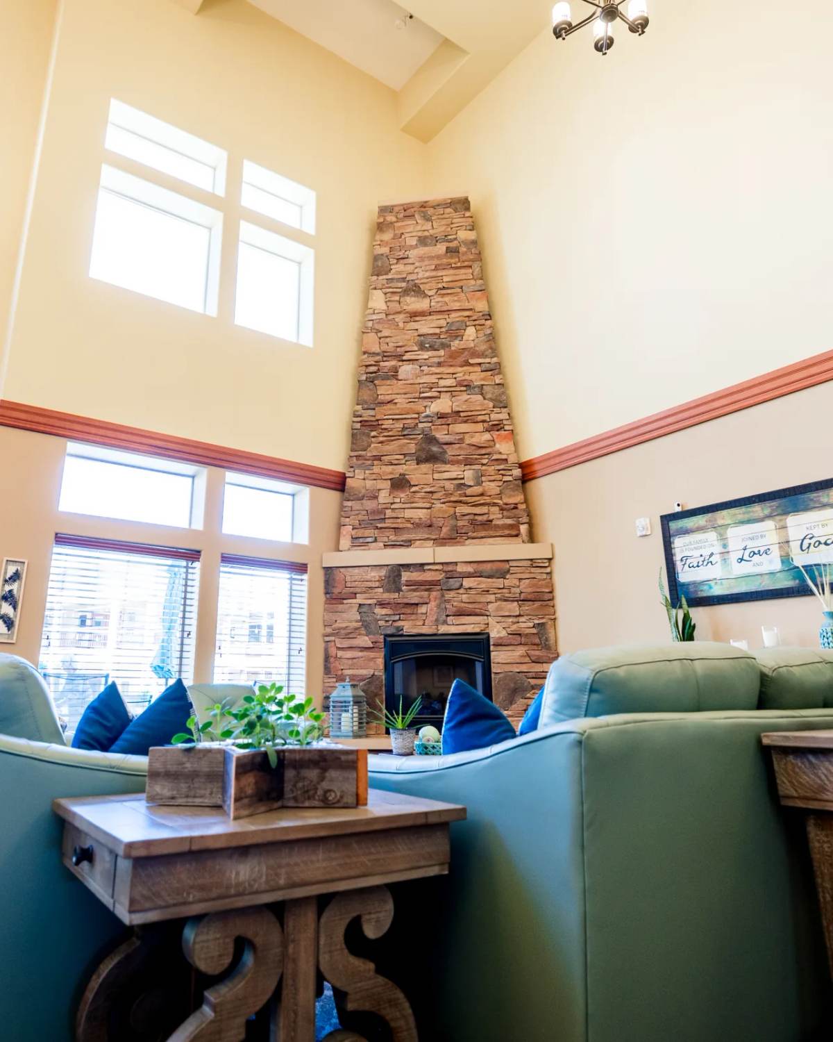 Gardens on Quail great room with tall stone fireplace, green sofas, and sunflowers