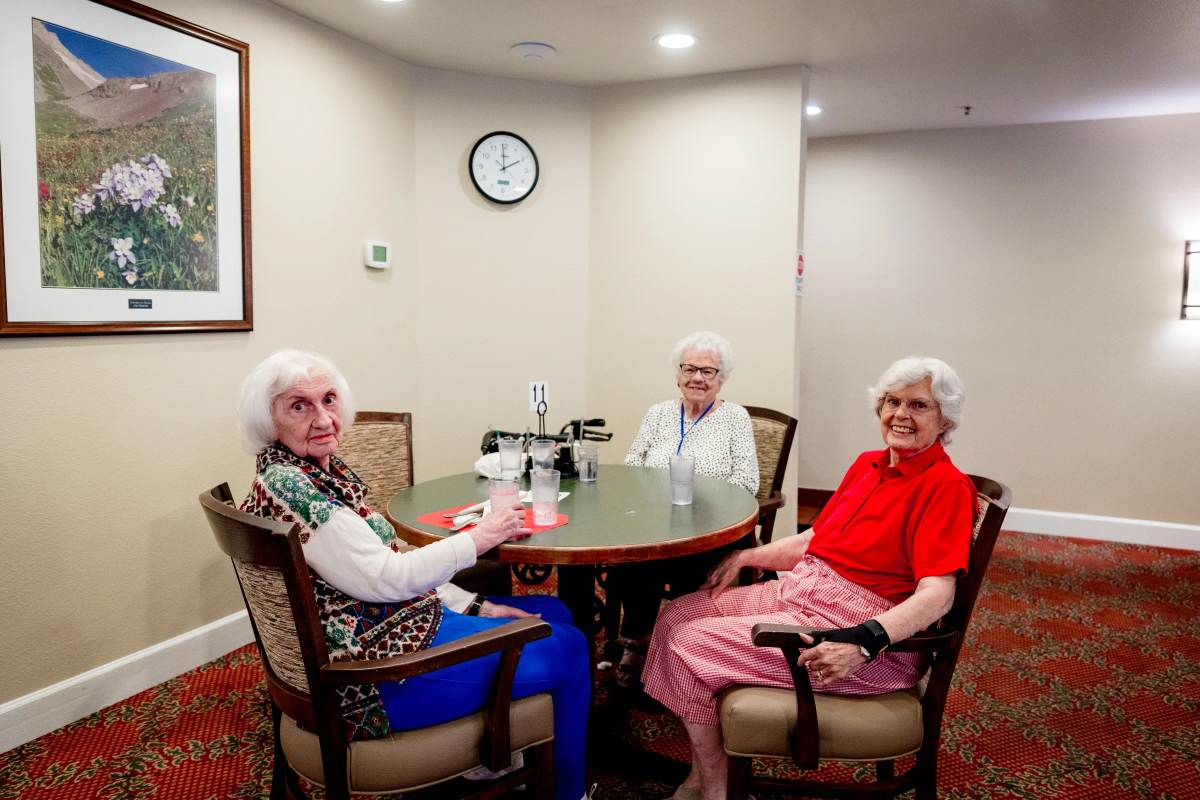 Three Gardens at Columbine residents at a dining table beneath mountain wildflower art