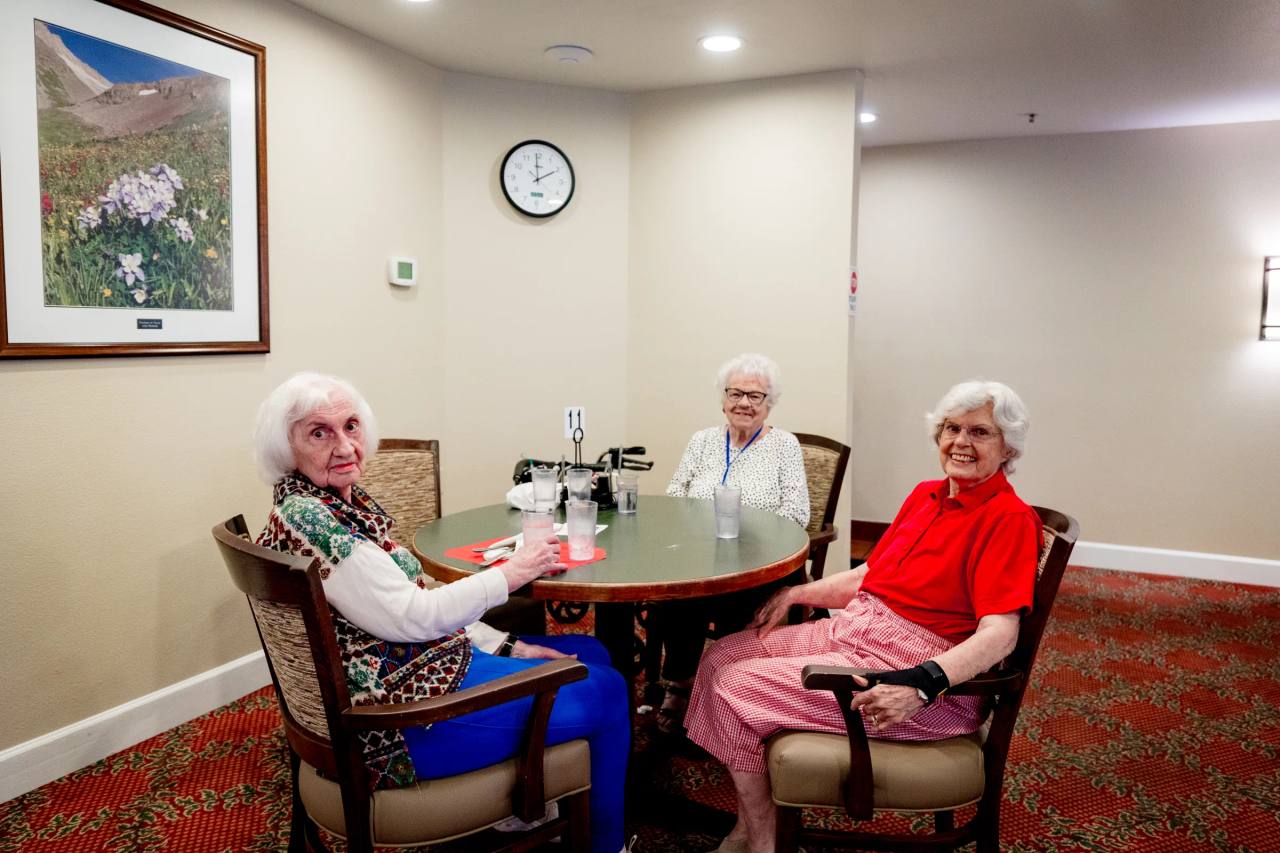 Three Gardens at Columbine residents at a dining table beneath mountain wildflower art