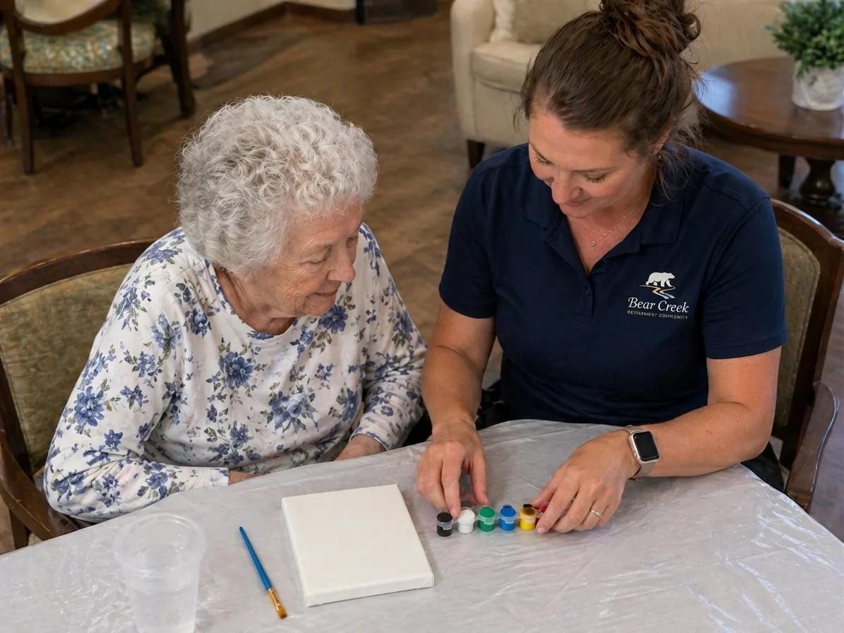 Bear Creek life enrichment staff member guiding a resident through a small-canvas painting activity with acrylic paints