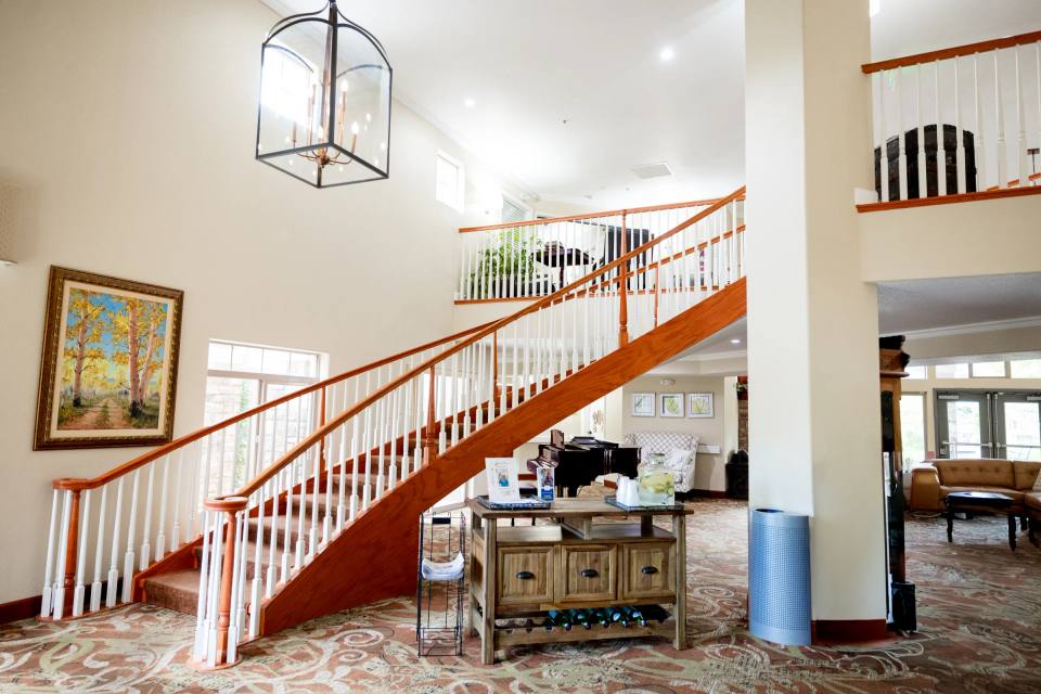 Golden Pond grand two-story foyer with wooden staircase, grand piano, and landscape painting