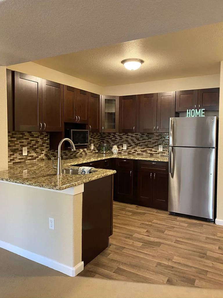 Golden Pond independent living apartment full kitchen with dark cabinets, granite counters, sink, and refrigerator