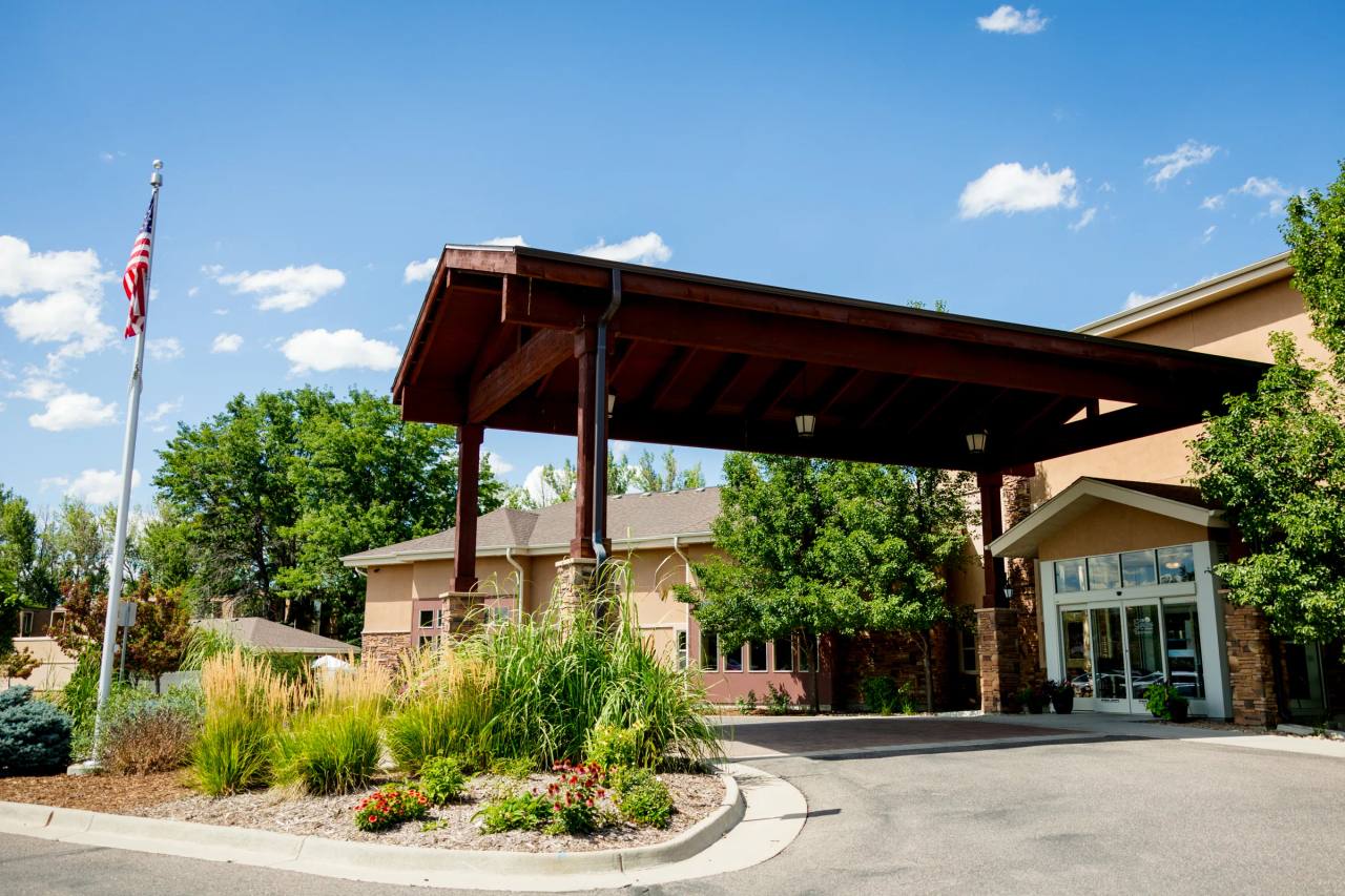 Gardens on Quail main entrance with wood porte-cochère, flag pole, and ornamental grasses