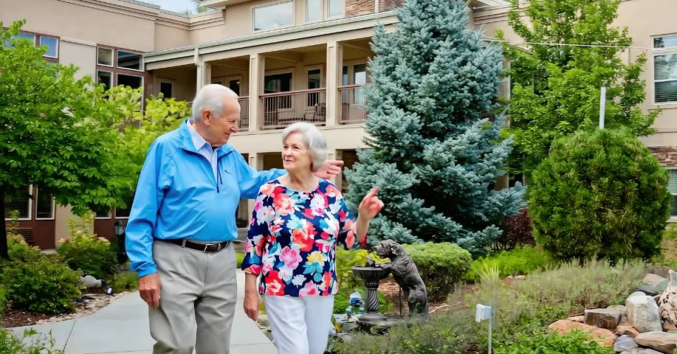 Gardens on Quail senior couple walking together through the landscaped courtyard near mature blue spruce
