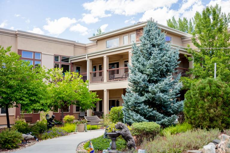 Gardens on Quail exterior with mature blue spruce and bronze bear sculpture