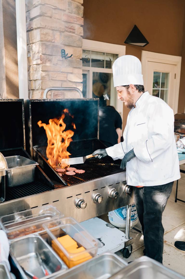 Golden Pond chef flame-grilling burgers at the outdoor grill during a community event