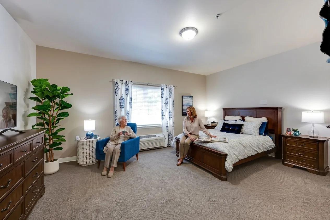 Bear Creek resident and visitor in a sunlit apartment bedroom with a queen bed and reading chair