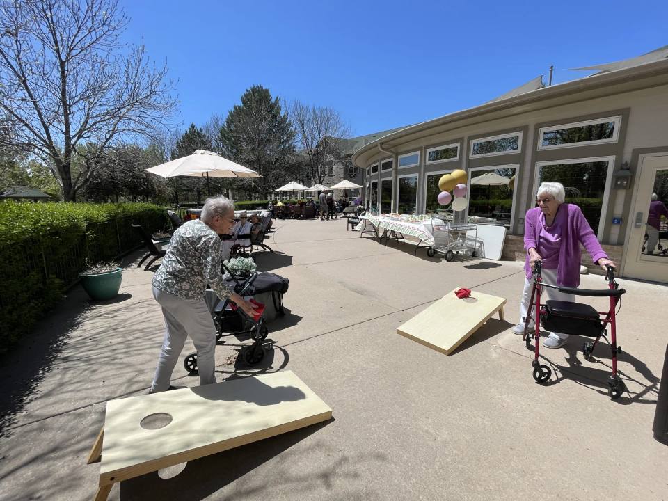 Gardens at Columbine residents playing cornhole on the sunny patio