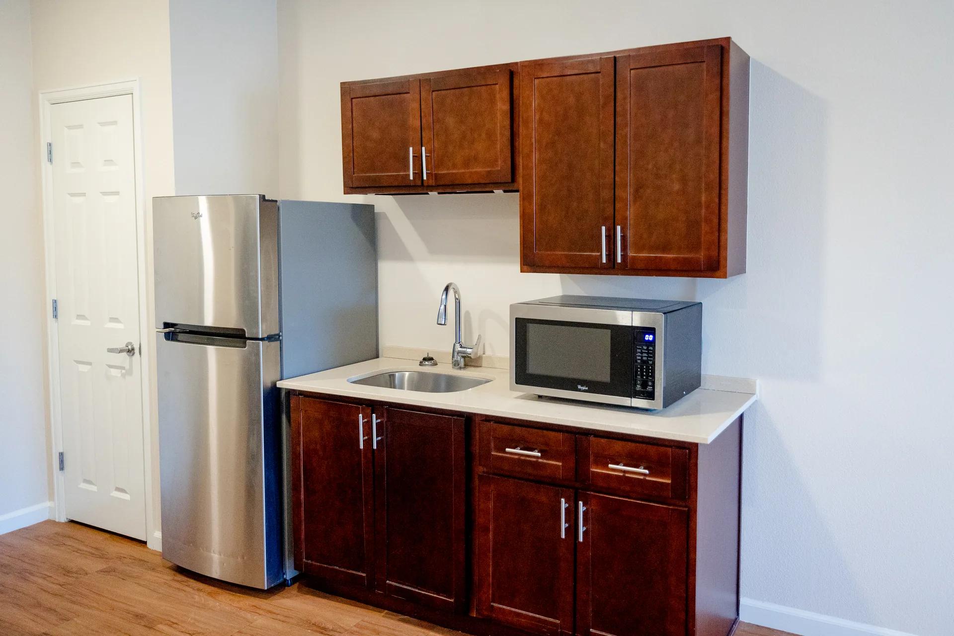 Stonebridge Senior apartment kitchenette with refrigerator, sink, microwave, and wood cabinets