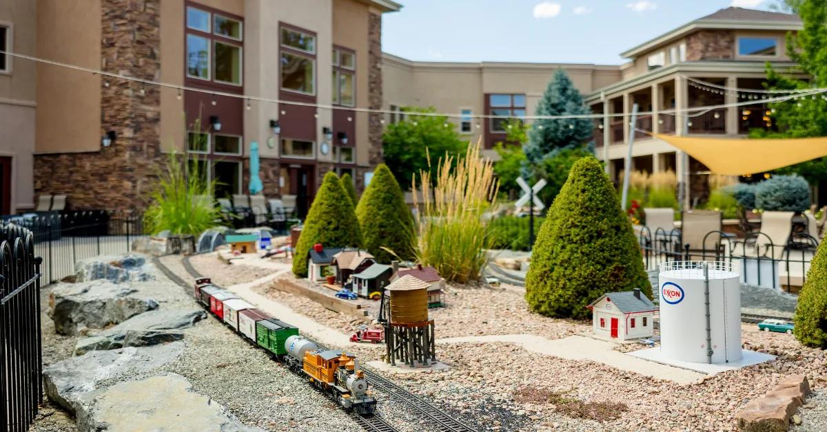 Gardens on Quail courtyard with model train garden, ornamental grasses, and residence building behind