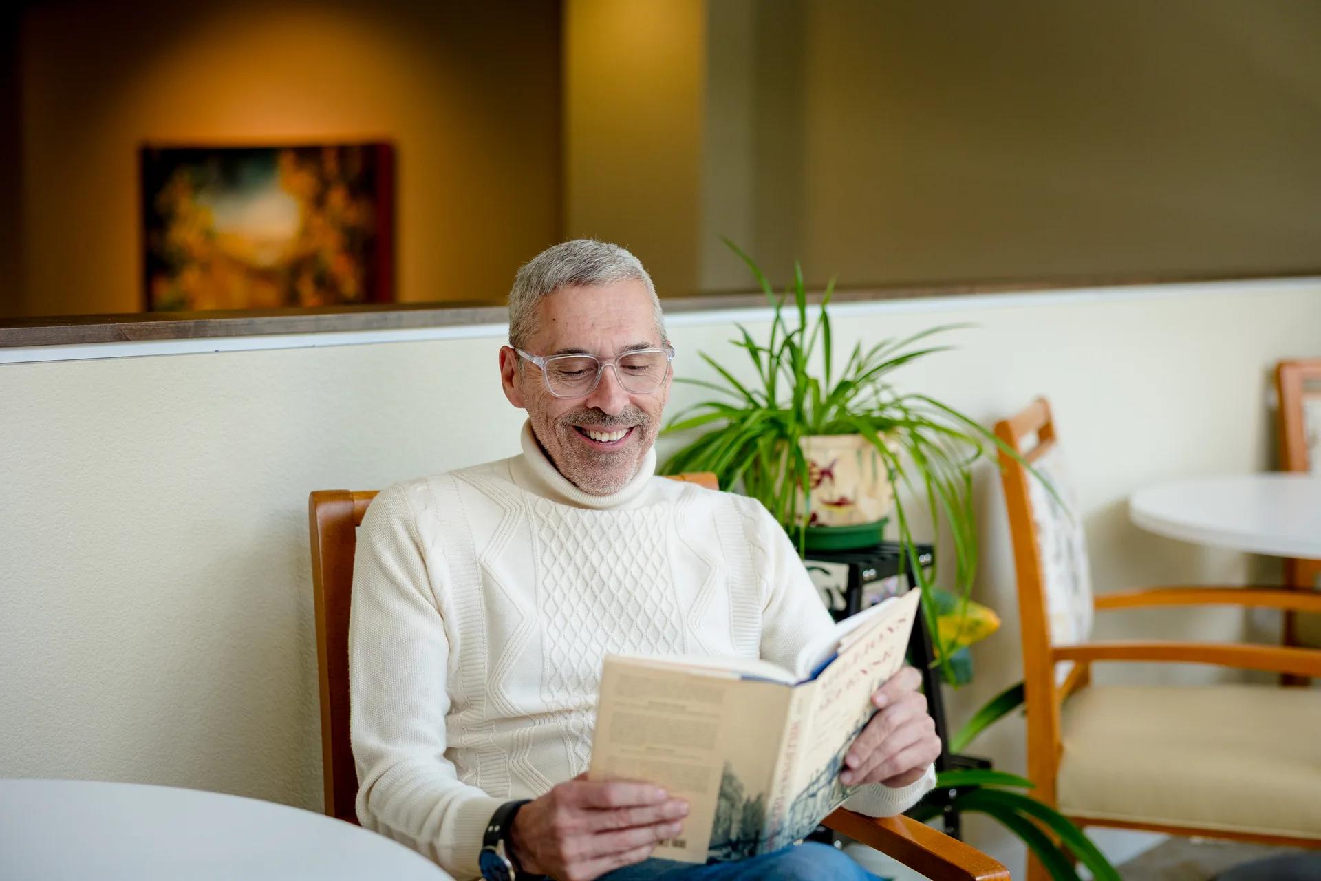 Stonebridge resident smiling while reading beside the sun deck plants