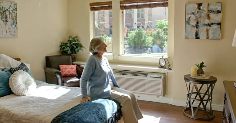 Gardens on Quail resident seated on the bed in a bright studio apartment with tall windows