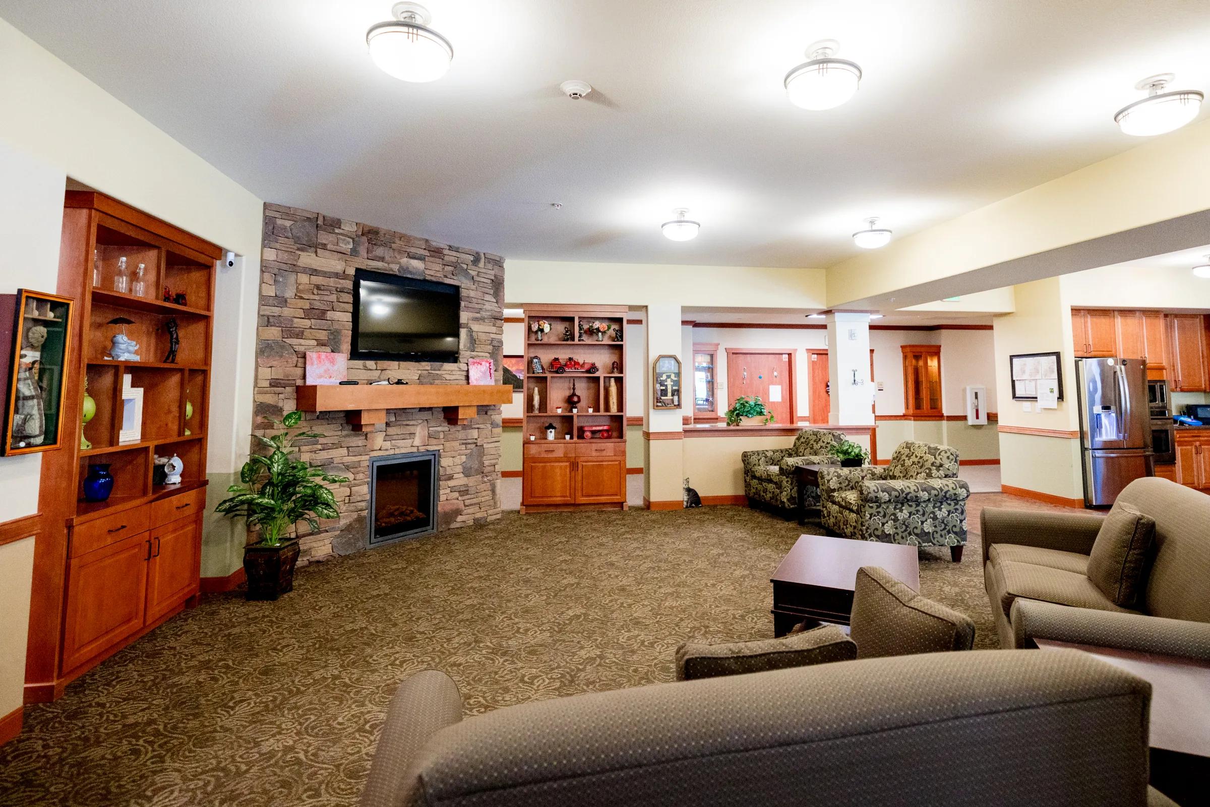Gardens on Quail memory care lounge with TV over stone fireplace and tan furniture