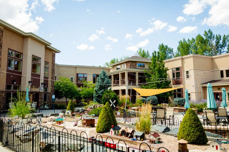 Gardens on Quail courtyard with model train garden, patio seating, and sun sail