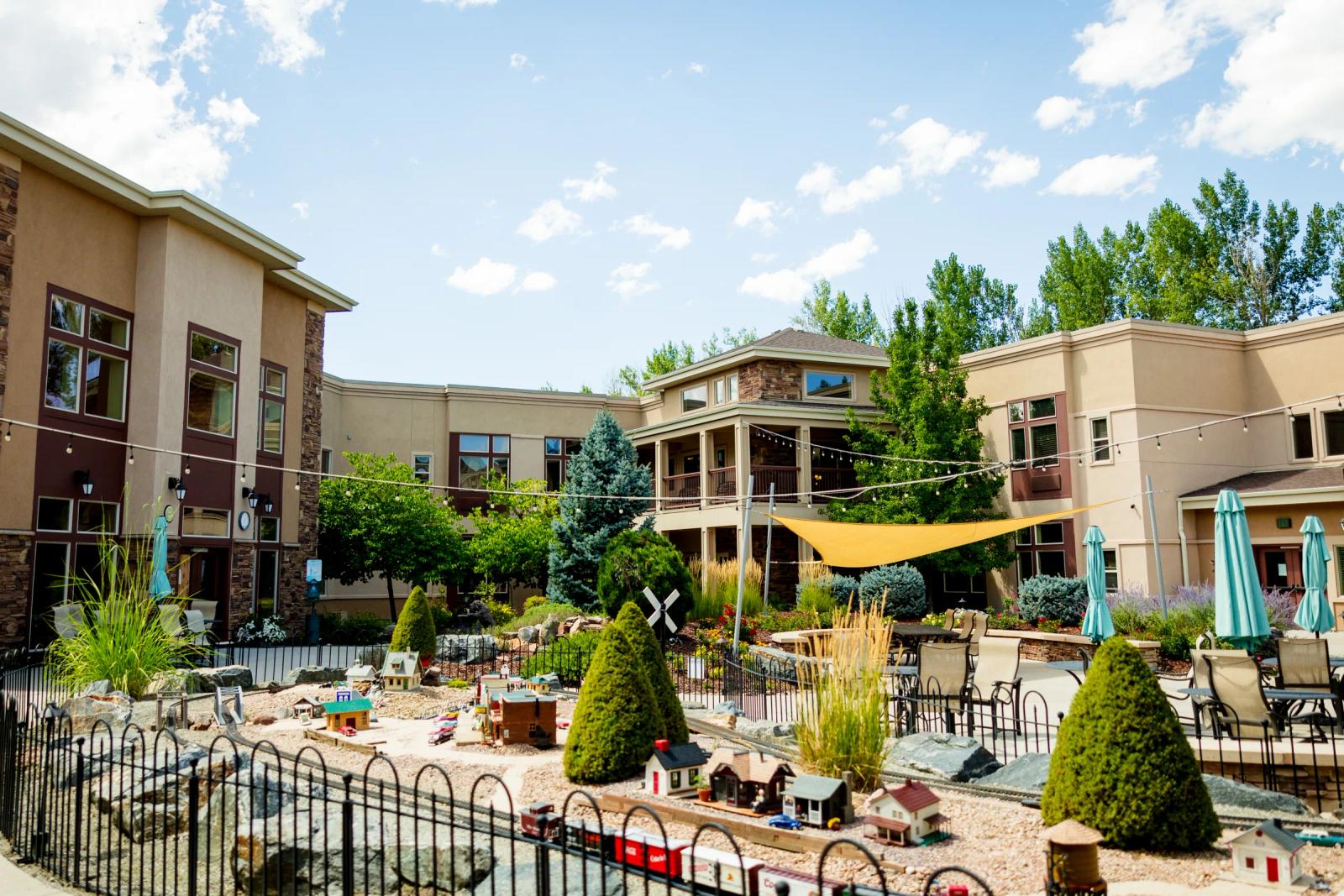 Gardens on Quail courtyard with model train garden, patio seating, and sun sail
