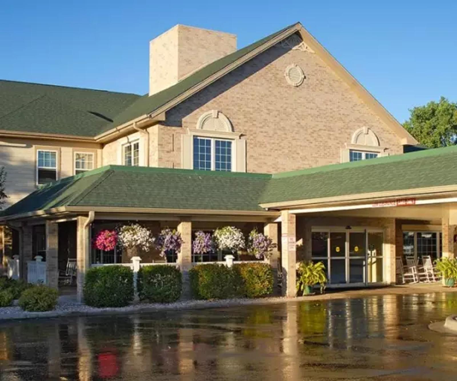 Exterior view of a brick building with a green roof and a covered entrance area with flowers.