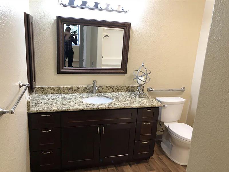 Golden Pond independent living apartment bathroom with wood vanity, granite counter, mirror, and support bars
