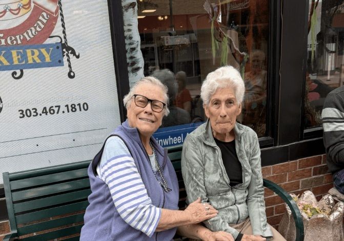 Two people seated together on a bench outside a shop.
