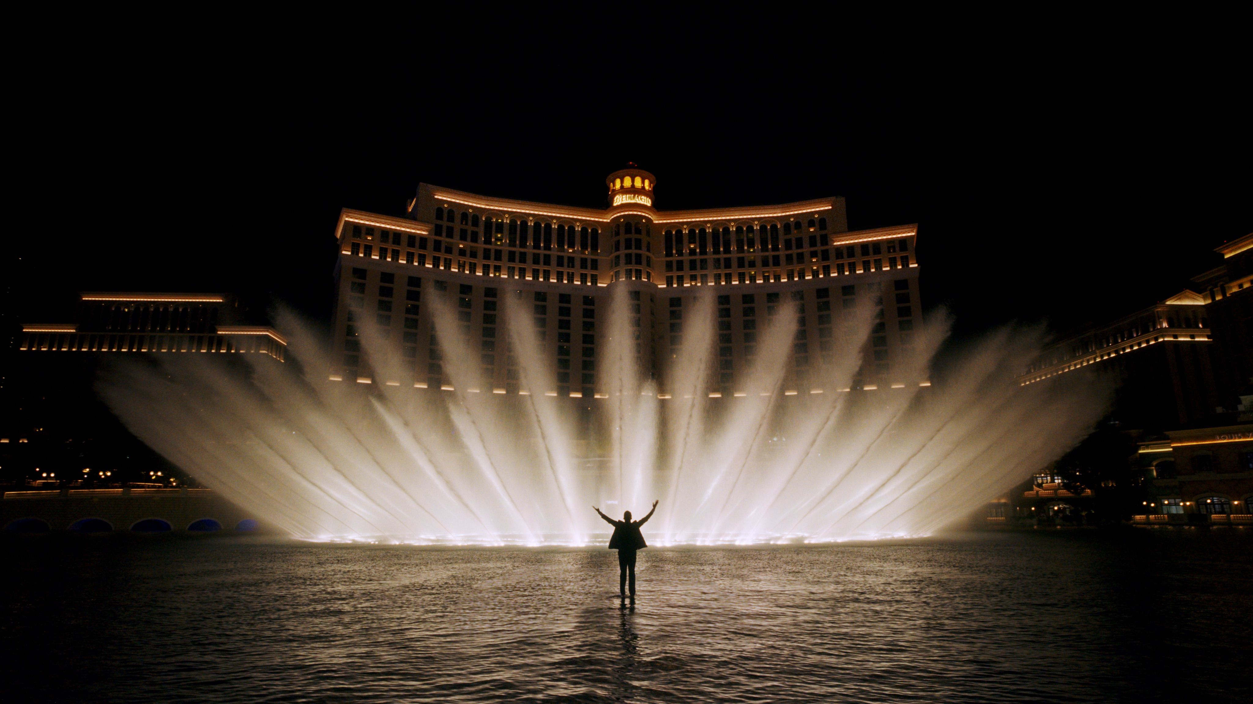 Man standing with his arms in the air in front of the Bellagio fountains