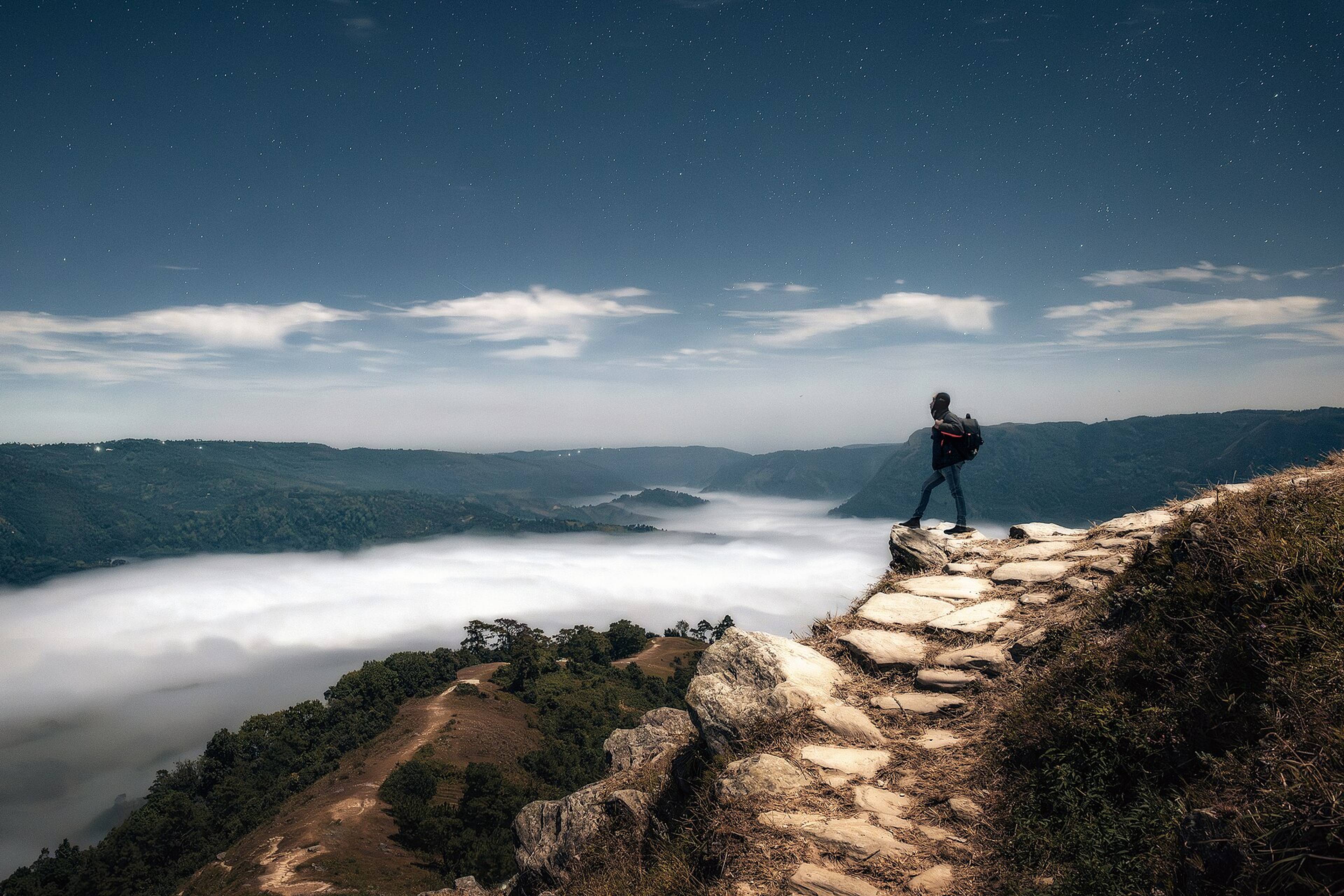 Hiker on a rocky ridge above a sea of clouds at Nongjrong, Meghalaya
