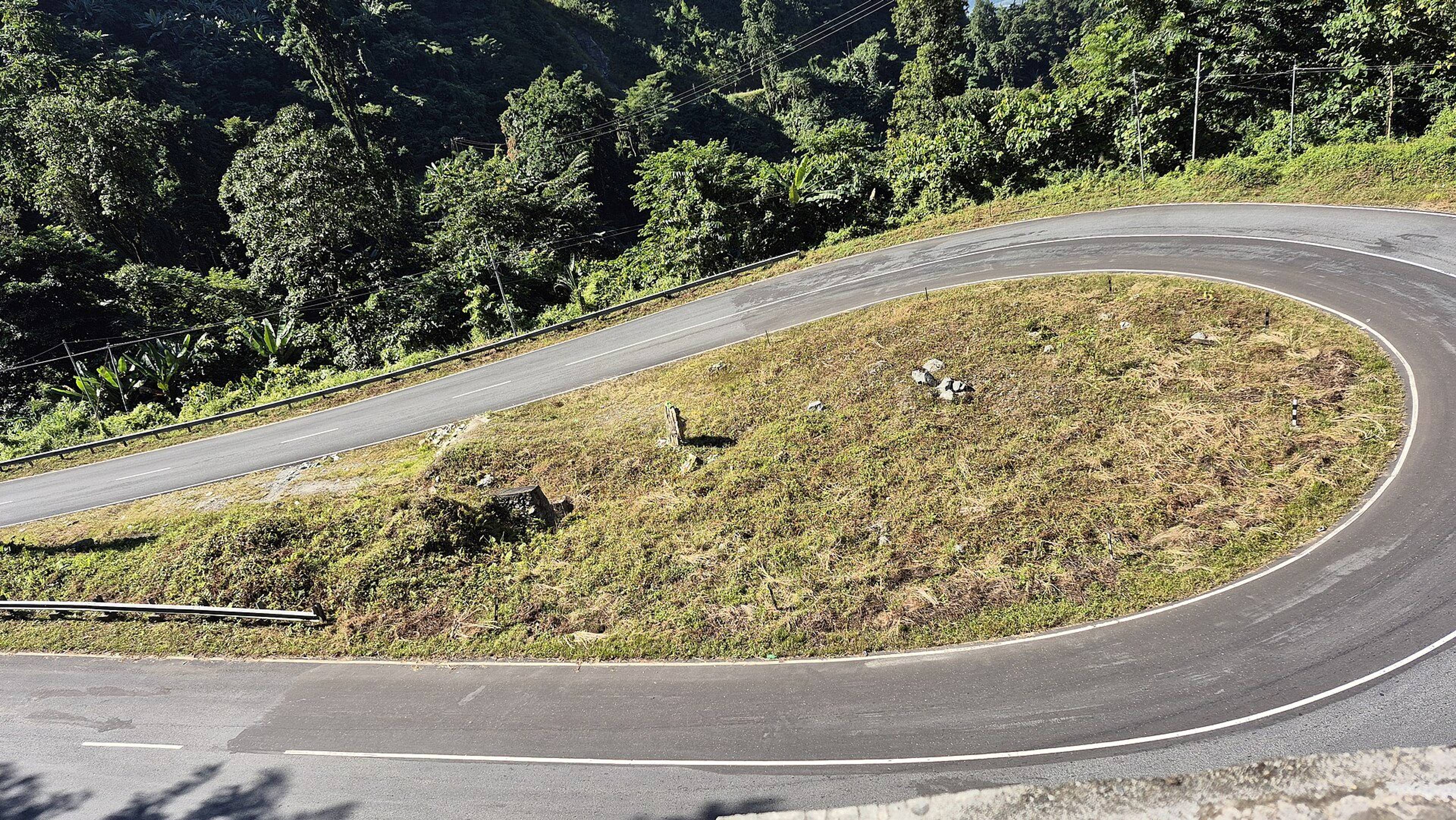A smooth mountain road with a sharp hairpin bend climbing towards Mayudia Pass through green hills