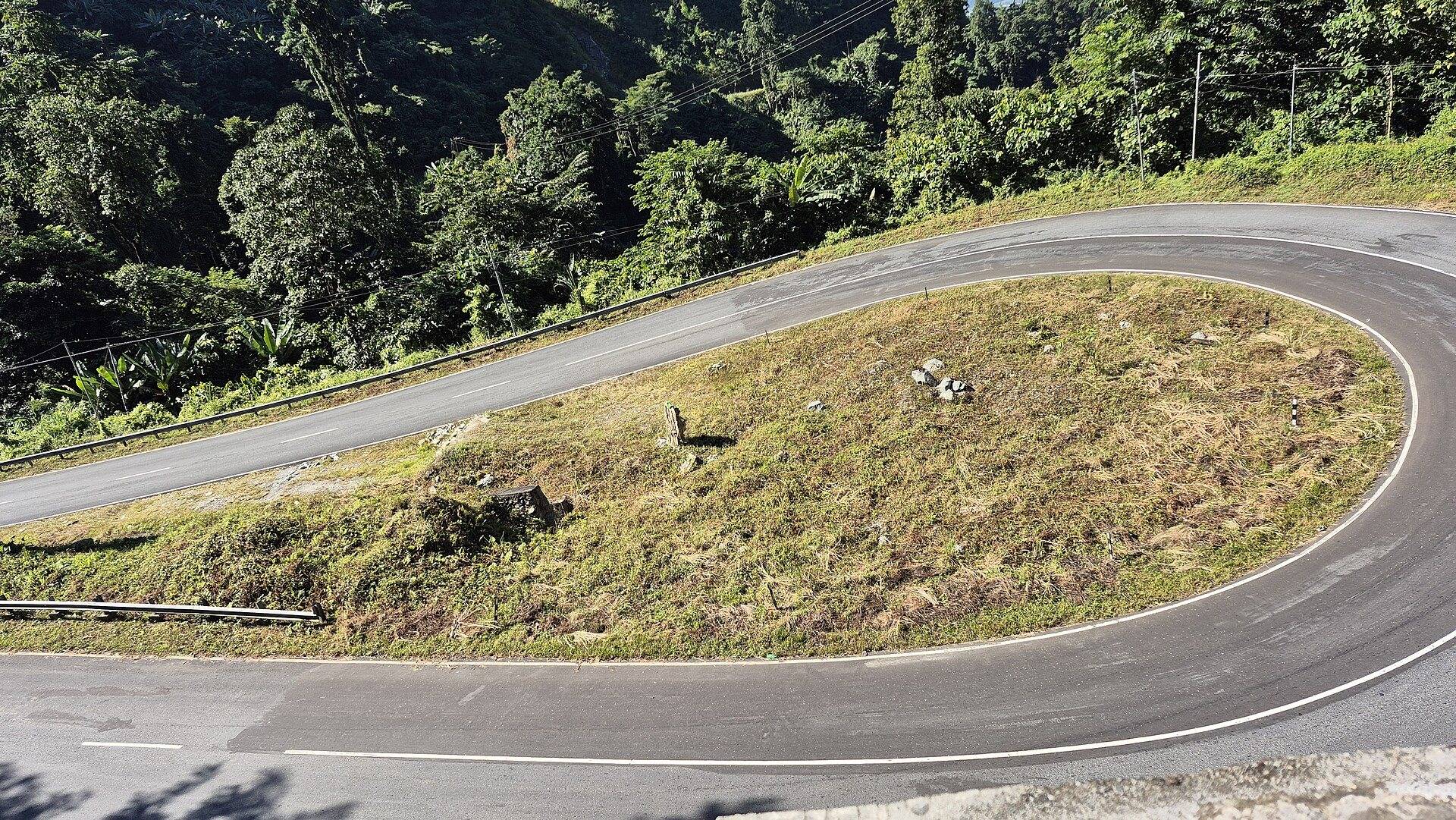 A smooth mountain road with a sharp hairpin bend climbing towards Mayudia Pass through green hills
