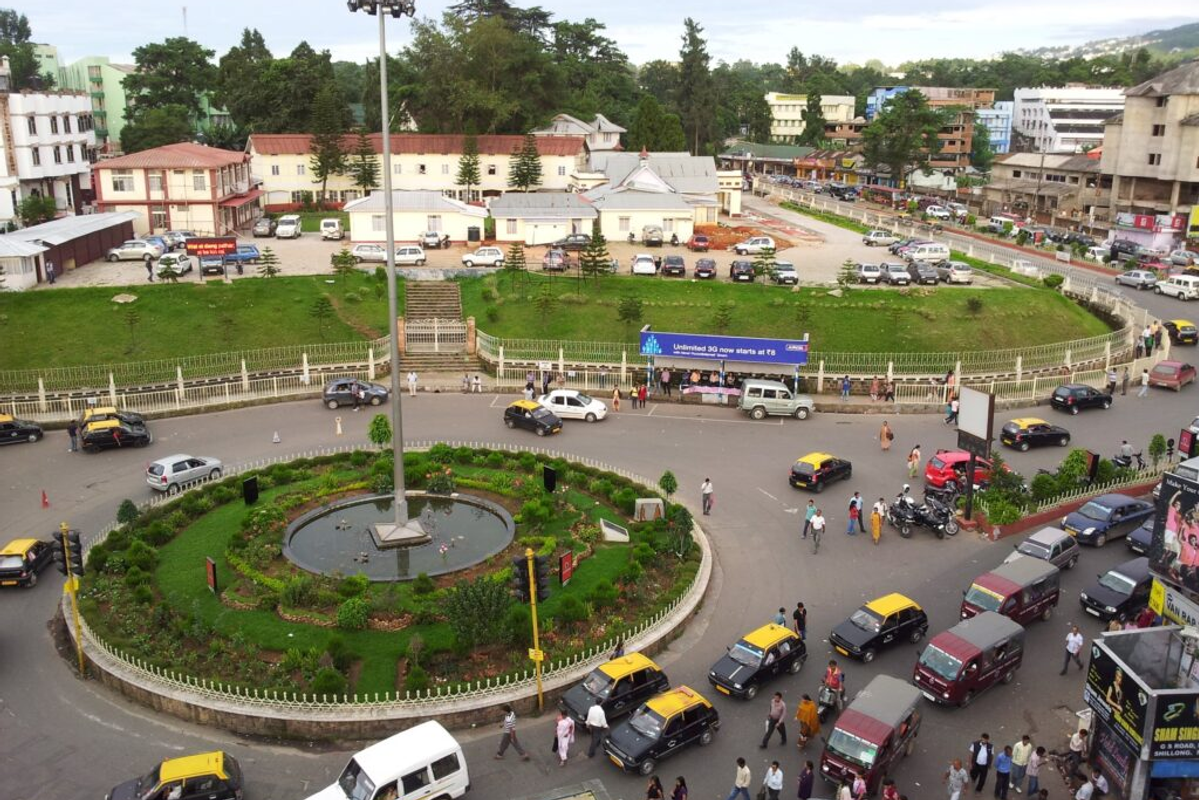 anoramic aerial view of Shillong city, Meghalaya, showing the dense residential buildings surrounded by lush green hills and a cloudy sky.