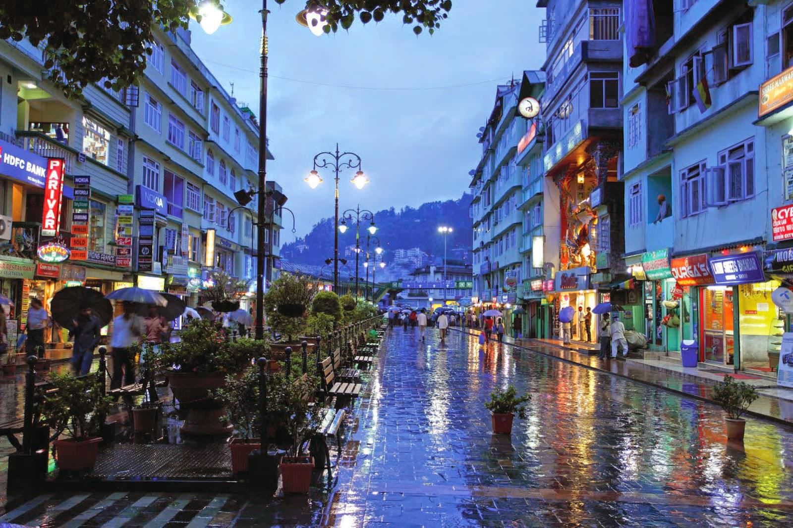 Tourists walking on the clean, pedestrianized MG Marg street in Gangtok with colorful shopfronts and benches at night.