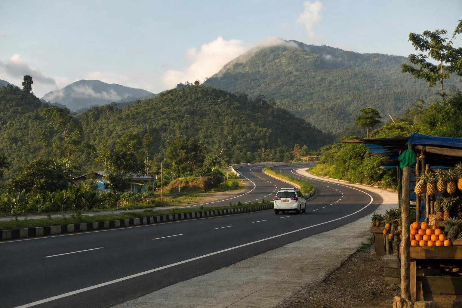 Highway winding through green forested hills on the drive from Guwahati to Shillong, with a roadside fruit stall