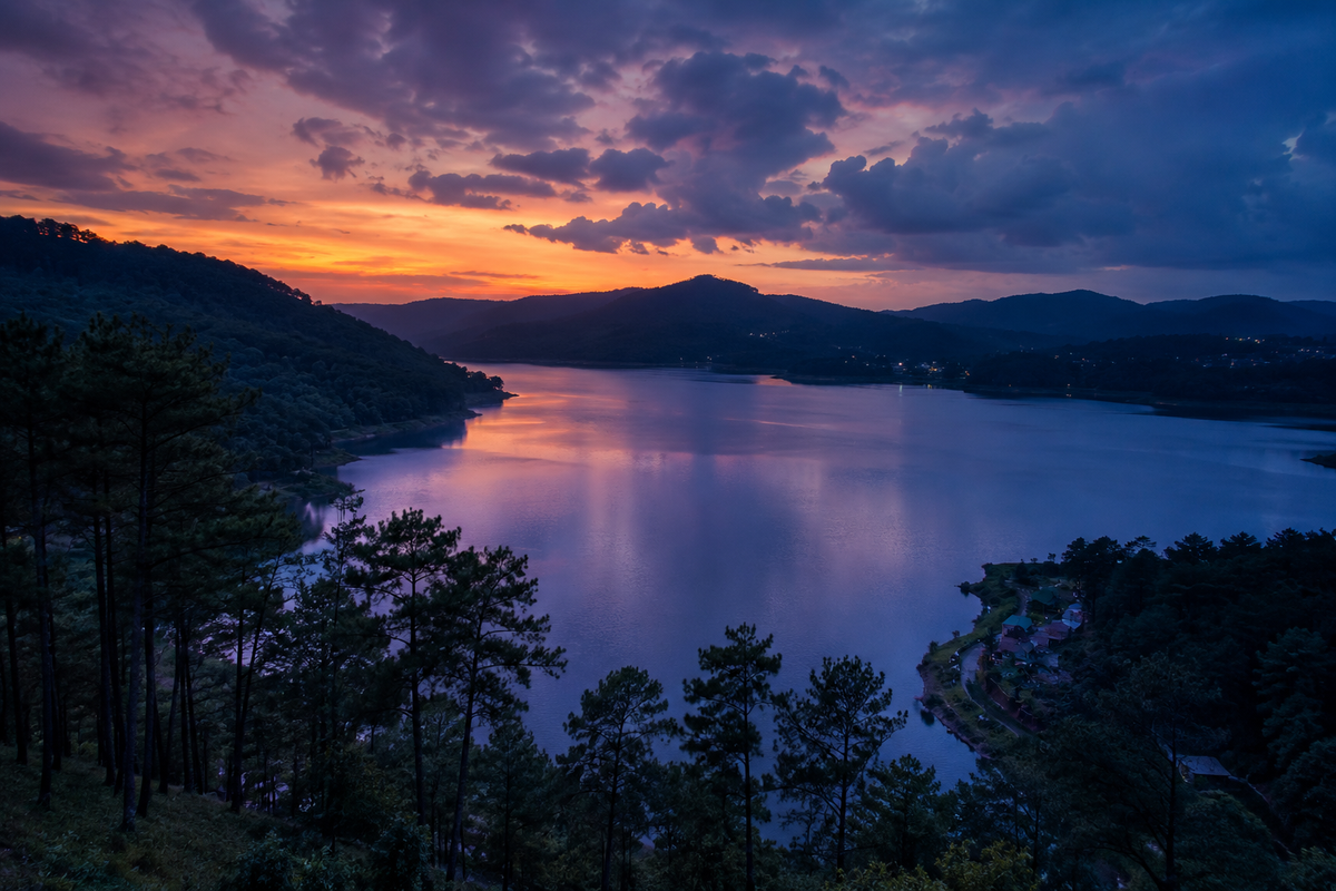 A cinematic twilight view of Umiam Lake in Meghalaya, showing calm water surfaces framed by dark pine forests.