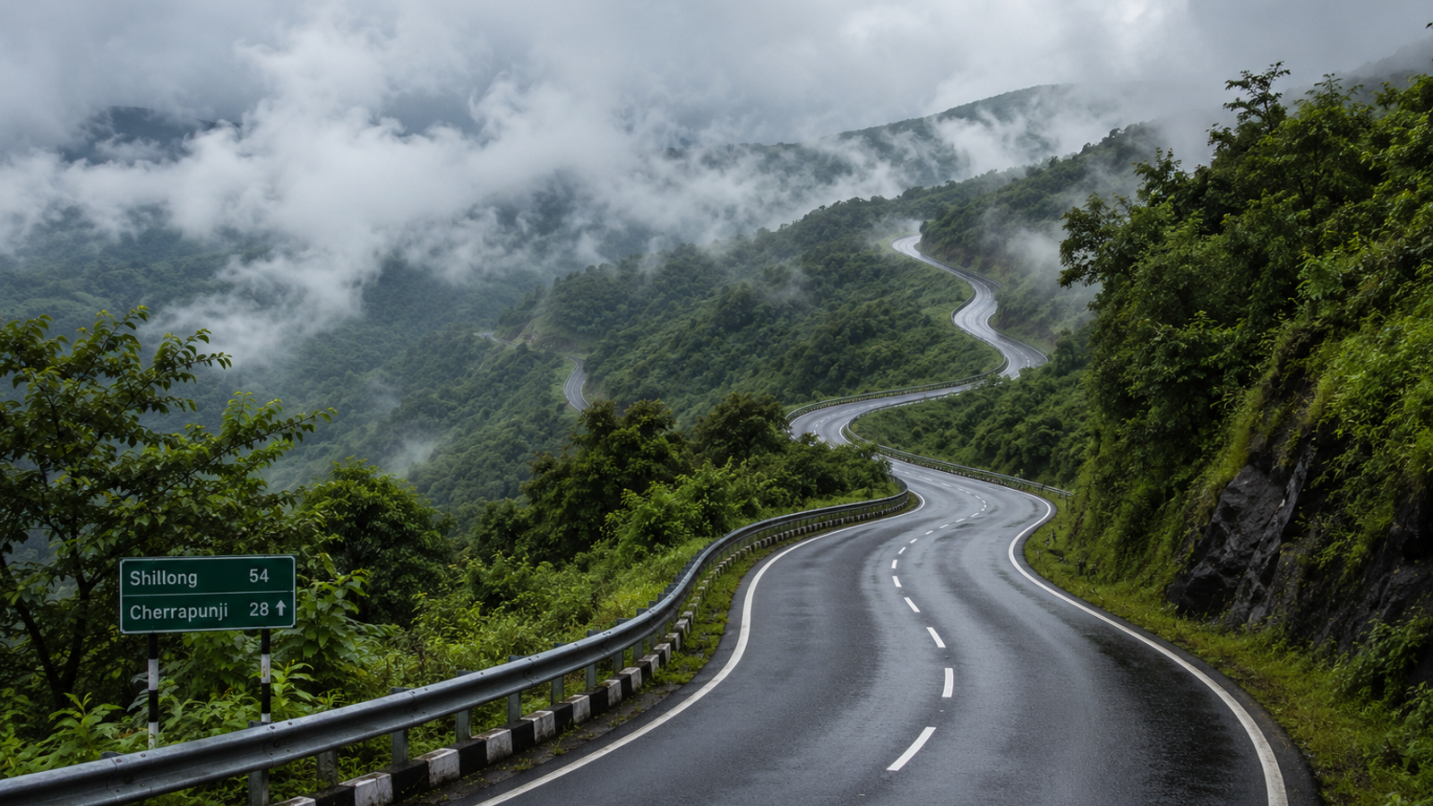 Winding two-lane asphalt highway on the road from Shillong to Cherrapunji flanked by lush green hills and rolling mist under a cloudy sky
