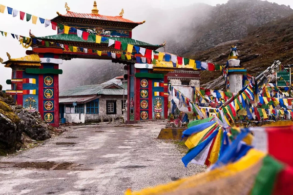 The colorful Tawang Welcome Gate adorned with vibrant red, blue, and white prayer flags against a backdrop of snow-capped mountains in Arunachal Pradesh.