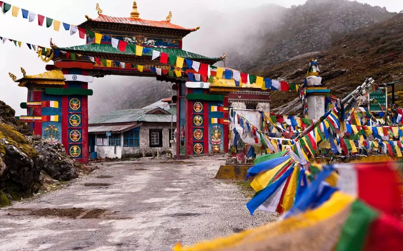 The colorful Tawang Welcome Gate adorned with vibrant red, blue, and white prayer flags against a backdrop of snow-capped mountains in Arunachal Pradesh.