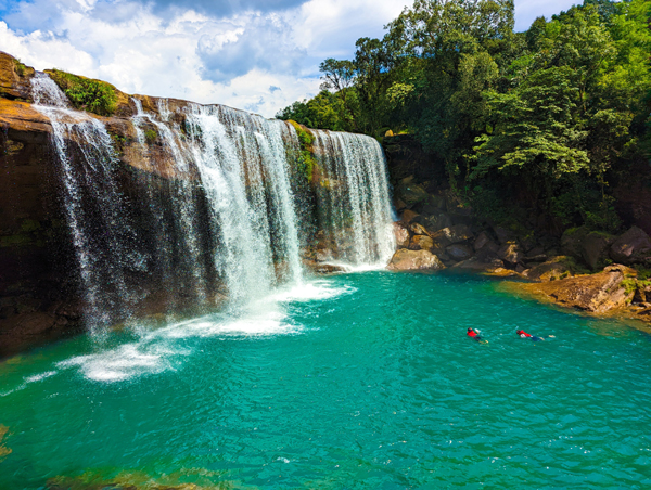 An action shot of a traveler wearing a bright orange life jacket swimming in the blue pool.