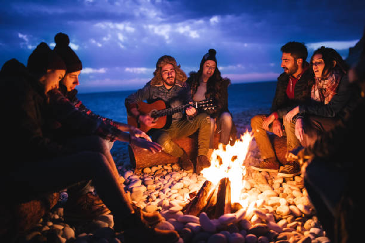 A group of travelers and musicians playing acoustic guitars around a campfire at a Ziro campsite.