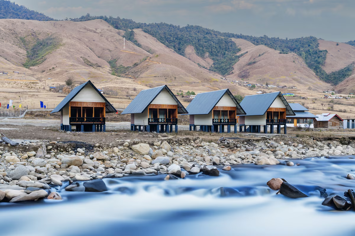 A cinematic boutique homestay in Mechuka valley, Arunachal Pradesh, surrounded by snow-capped mountains and pine forests.