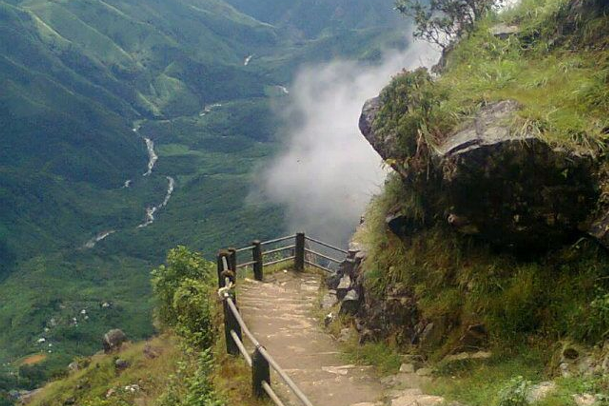 A wide landscape shot of Laitlum Canyon — deep misty gorges, layered green terraced valleys, and the East Khasi Hills stretching into the horizon at sunrise.