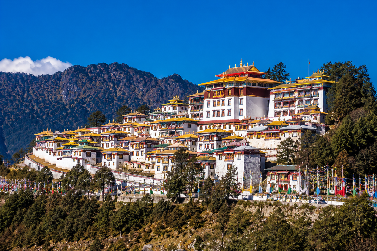 The grand and colorful buildings of the ancient Tawang Monastery sitting on a high mountain ridge under a clear sky.