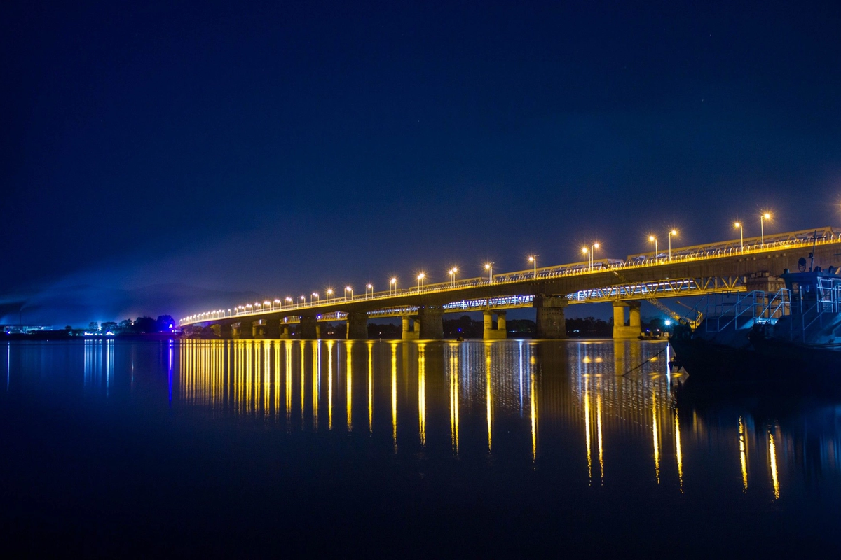 Saraighat Bridge over Brahmaputra River at night with city lights reflected in water Guwahati