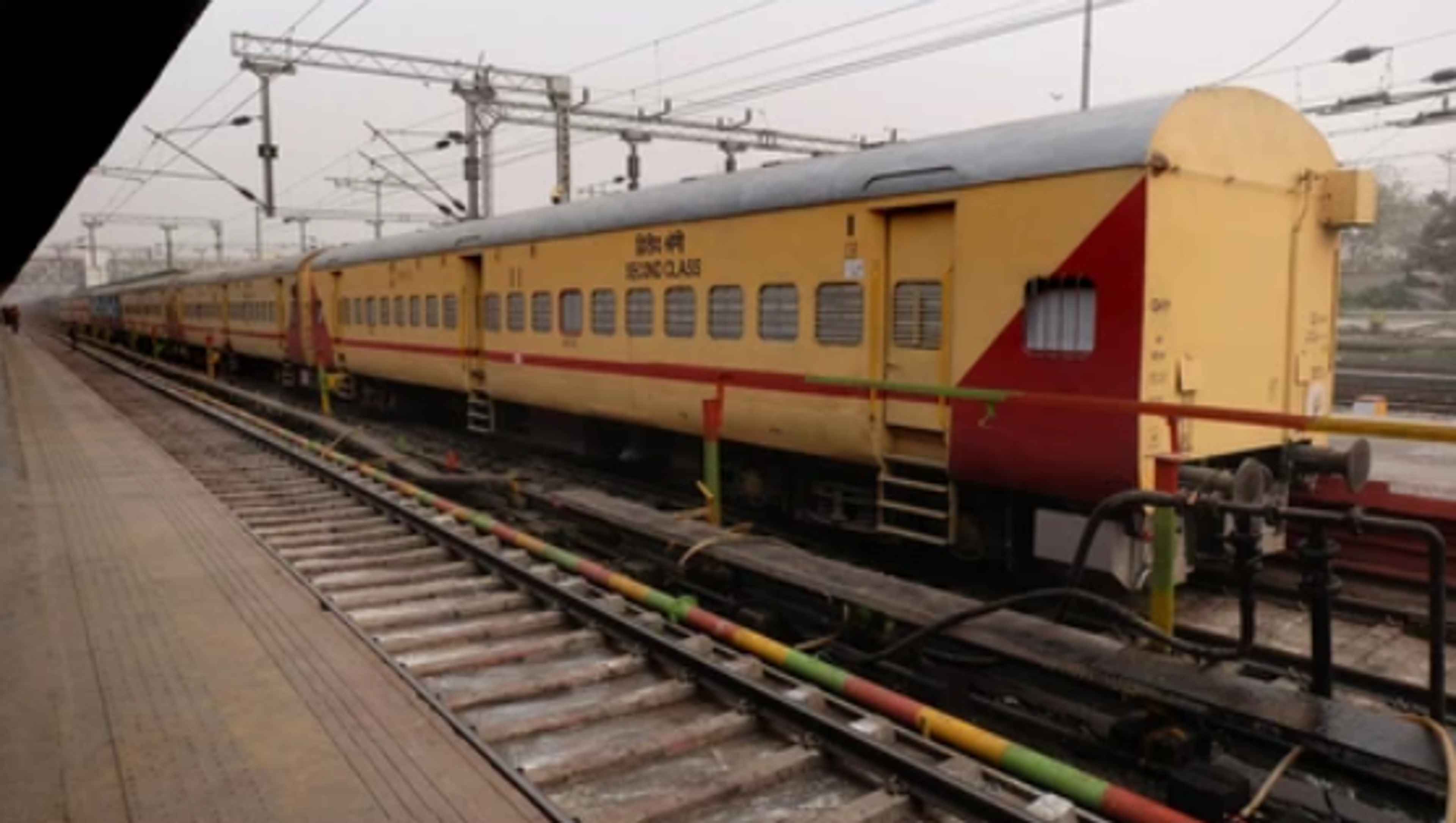 A view of a yellow and red express train standing at the platform of Guwahati railway station.