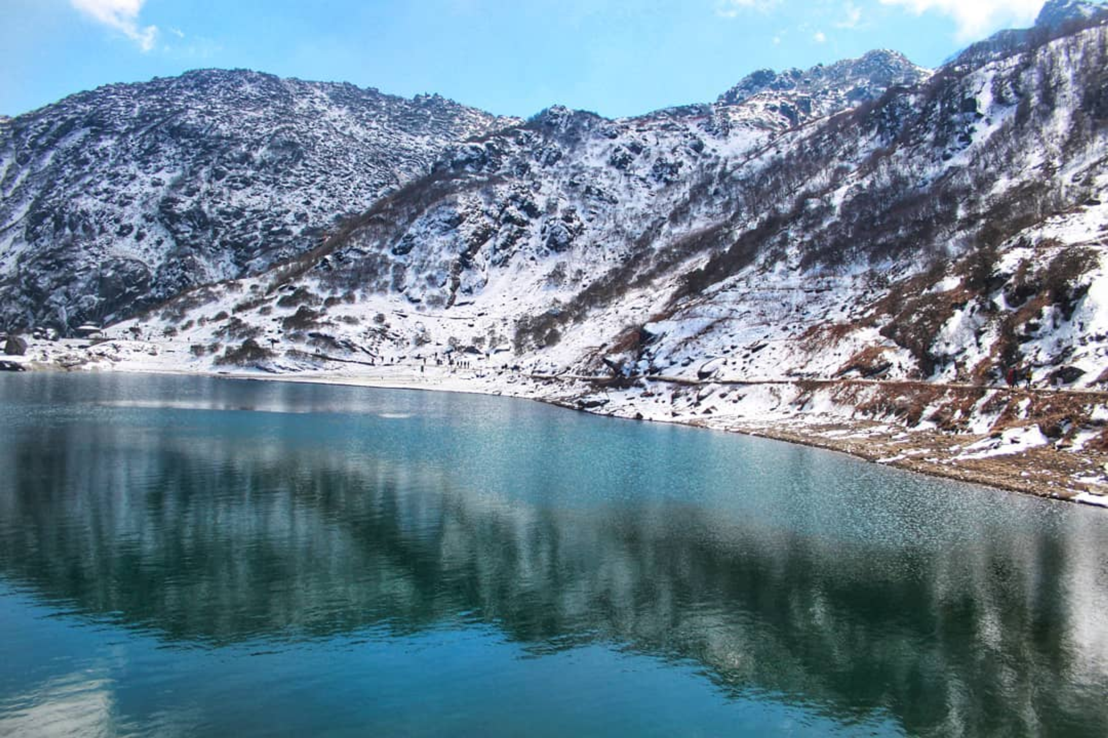 Turquoise Tsomgo Lake in Gangtok Sikkim surrounded by snow-capped Himalayan mountains and prayer flags.