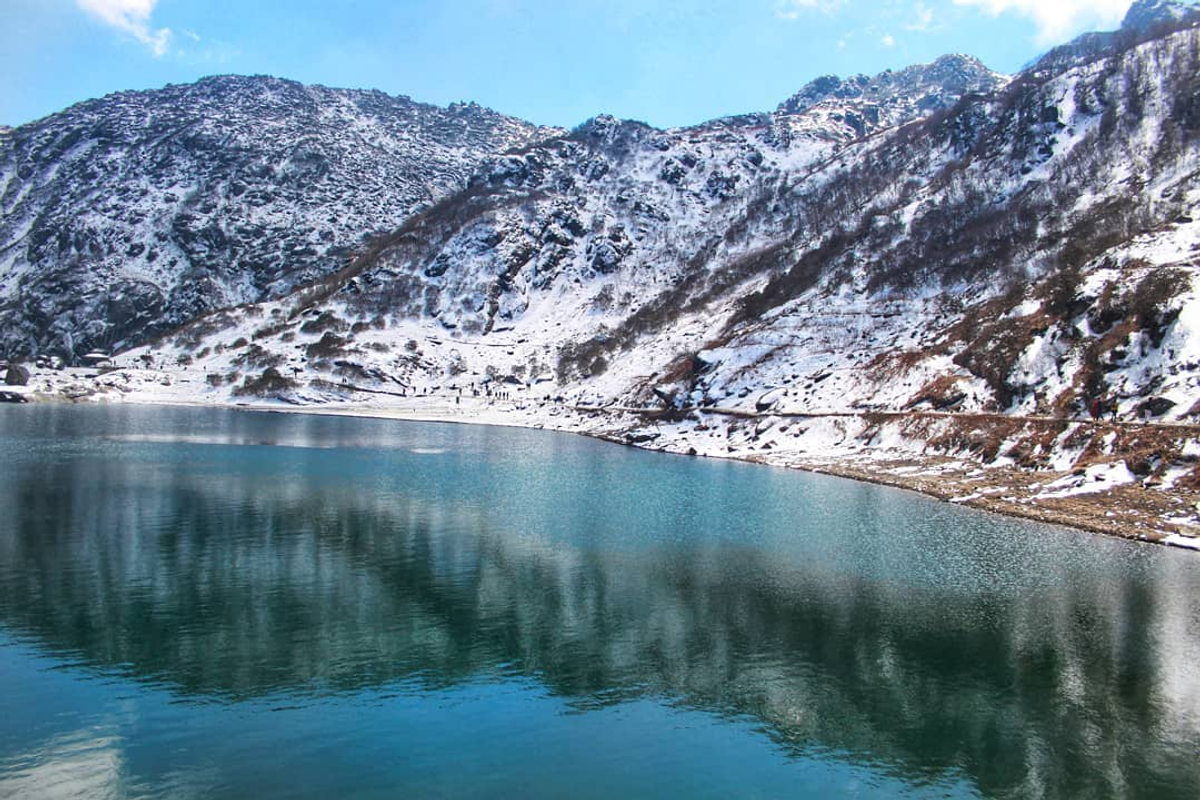 Turquoise Tsomgo Lake in Gangtok Sikkim surrounded by snow-capped Himalayan mountains and prayer flags.