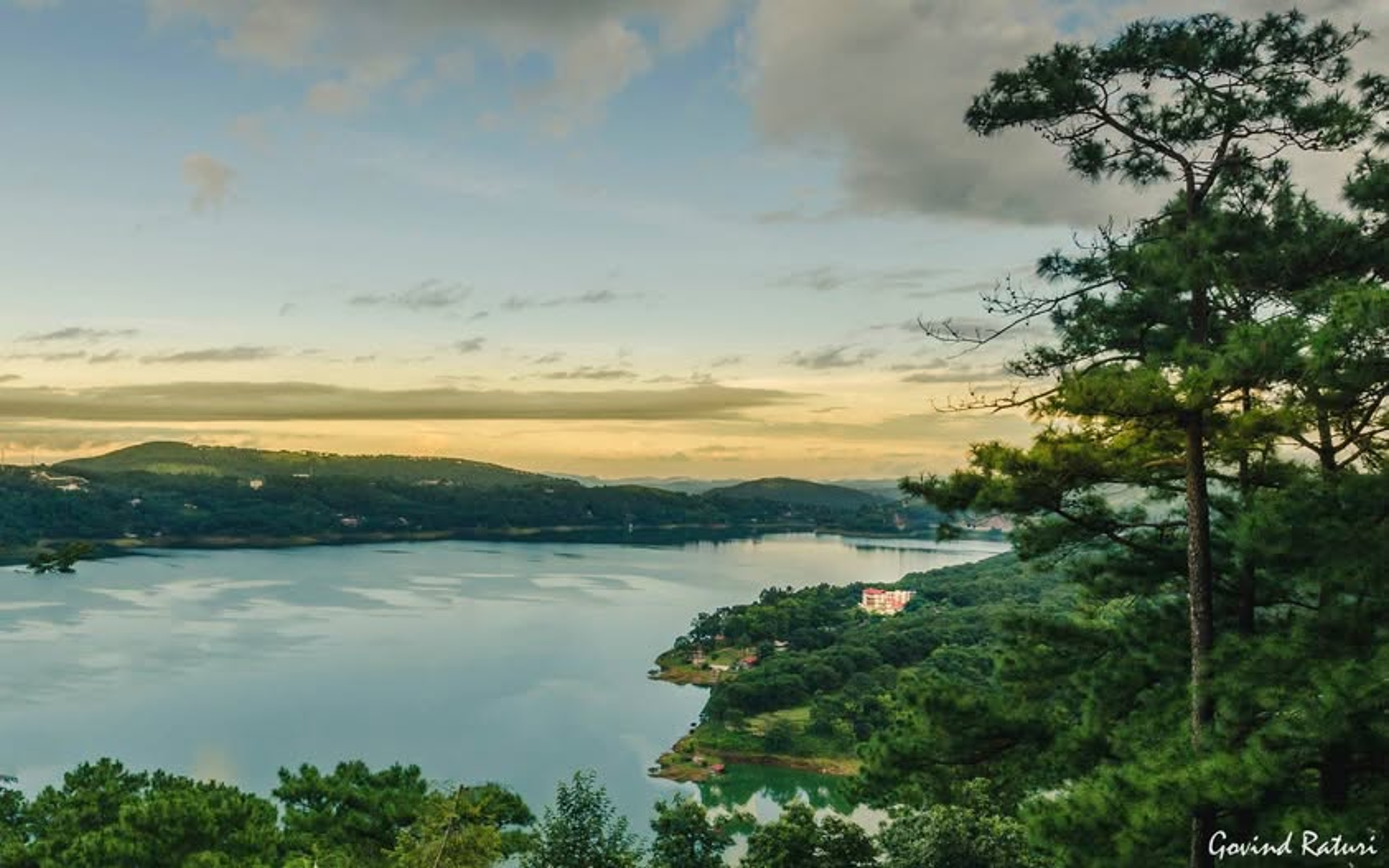 A panoramic shot of the deep blue waters of Umiam Lake in Meghalaya surrounded by green pine forests under a bright afternoon sun