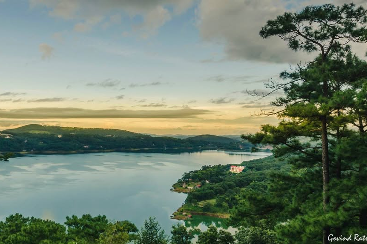 A panoramic shot of the deep blue waters of Umiam Lake in Meghalaya surrounded by green pine forests under a bright afternoon sun
